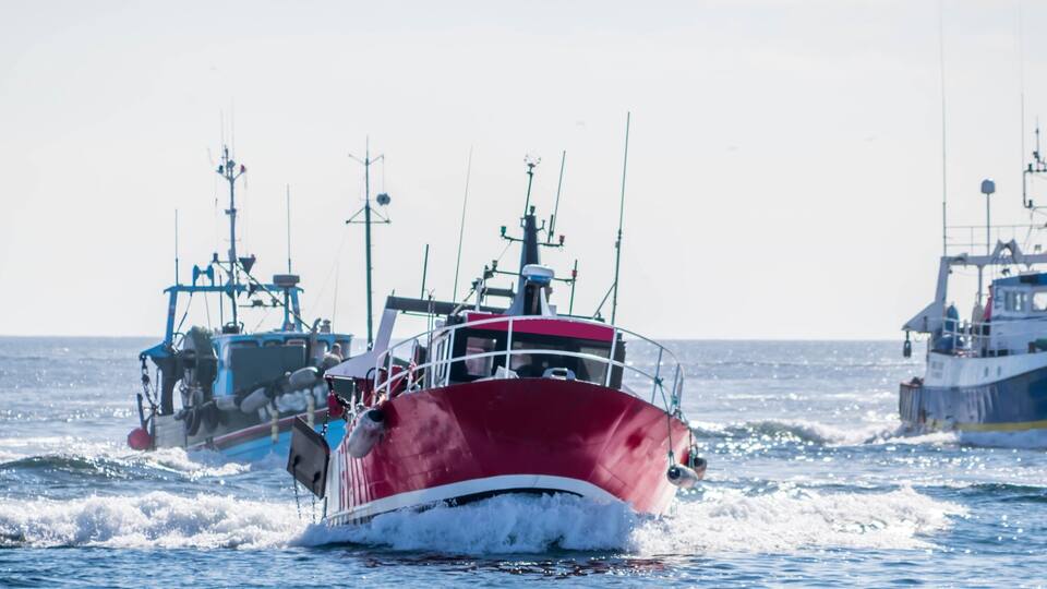 A red boat moving through the water with other boats in the background.