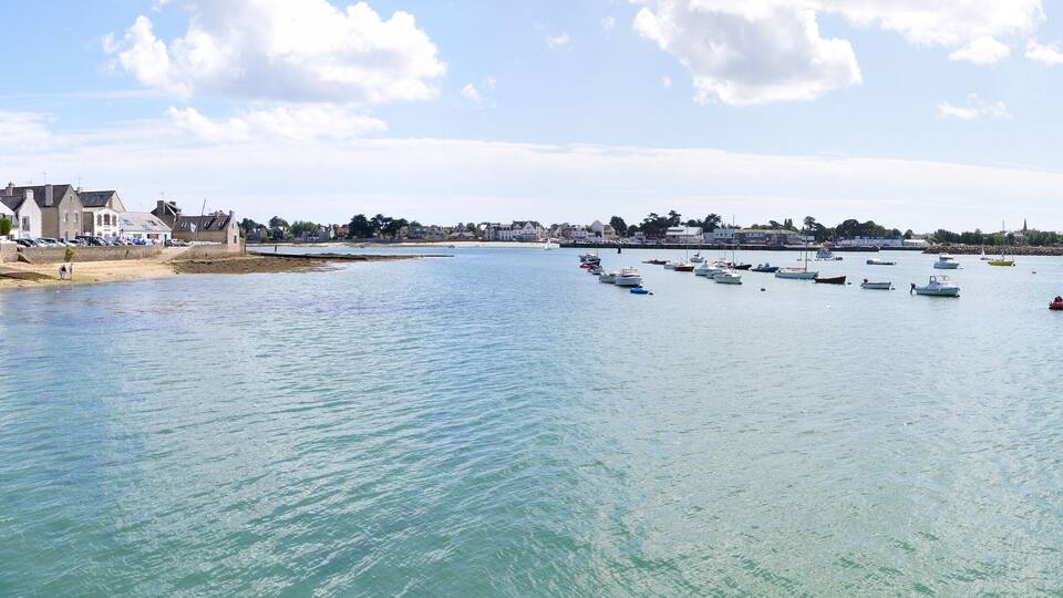 A coastal town with a clear blue sea, boats, and buildings along the shore.
