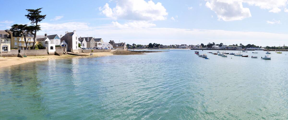 A coastal town with a clear blue sea, boats, and buildings along the shore.