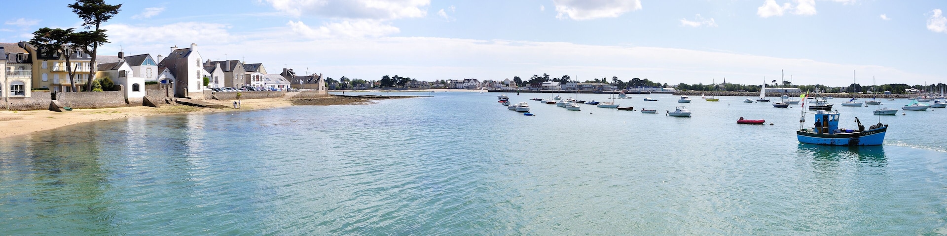 A coastal town with a clear blue sea, boats, and buildings along the shore.