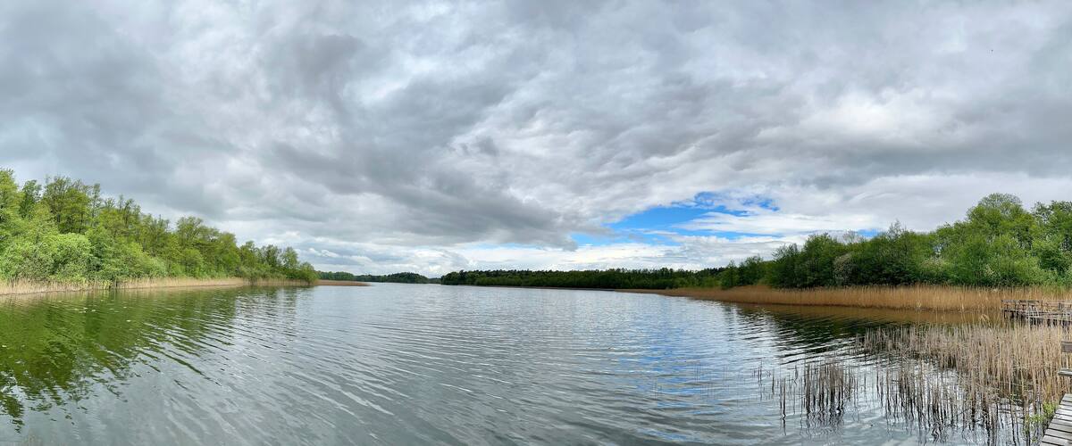 A calm river with dense greenery on both sides and a cloudy sky.