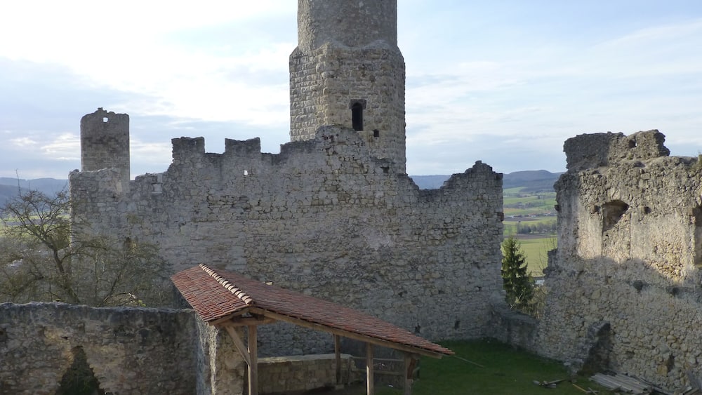 Un château médiéval en pierre, doté d’une tour, de ruines et d’une petite construction en bois.
