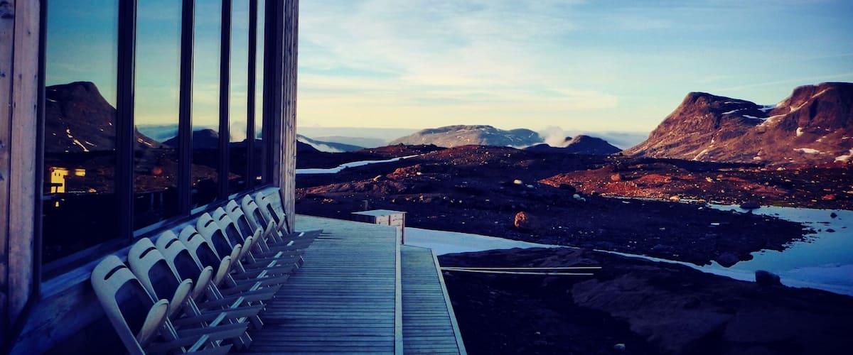 A wooden building with large windows overlooking a mountainous landscape with a lake.