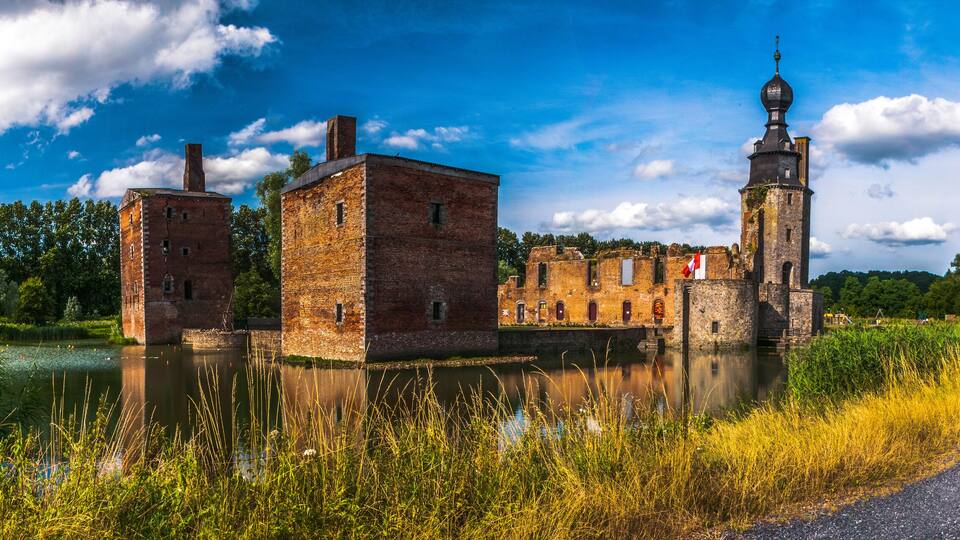 A historic building complex with a tower and a river in the foreground.