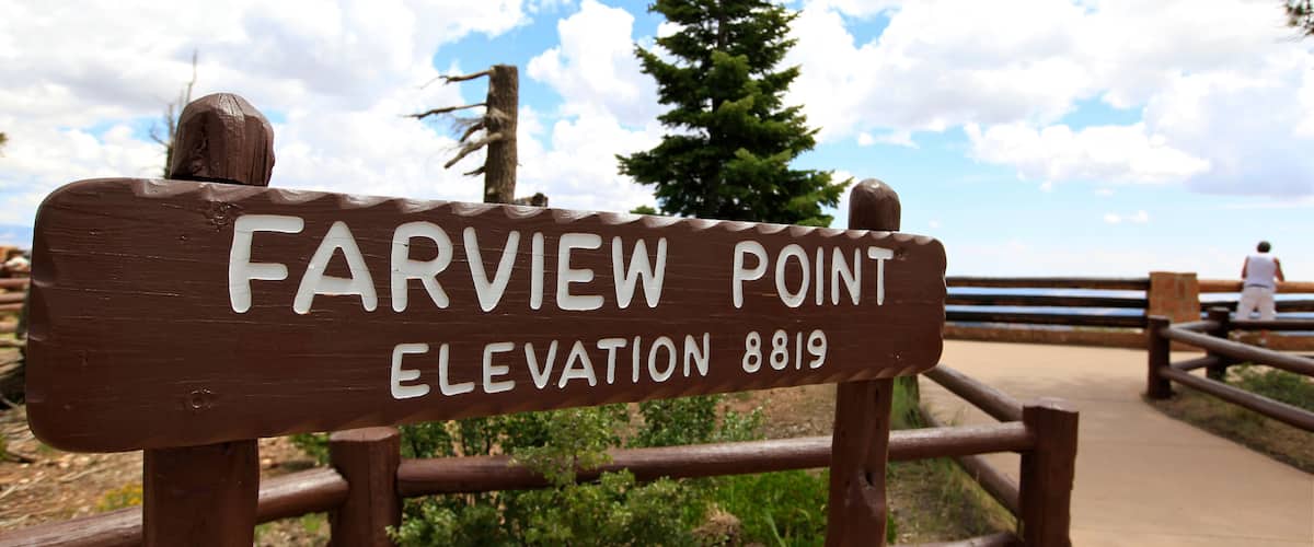 A sign reading "Farview Point Elevation 8819" with a wooden fence and a person in the background.