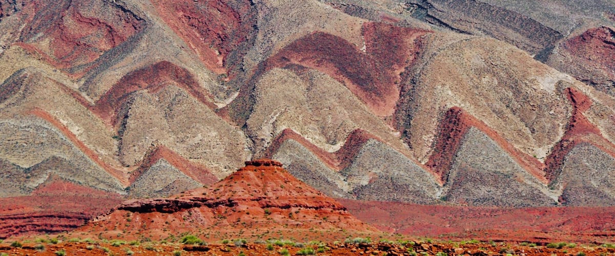 A layered rock formation with distinct red, orange, and beige strata.