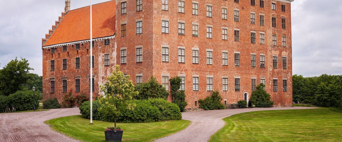 A large brick building with a red-tiled roof, surrounded by well-maintained lawns and trees.