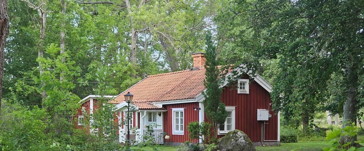 A red wooden house with a tiled roof surrounded by lush greenery.