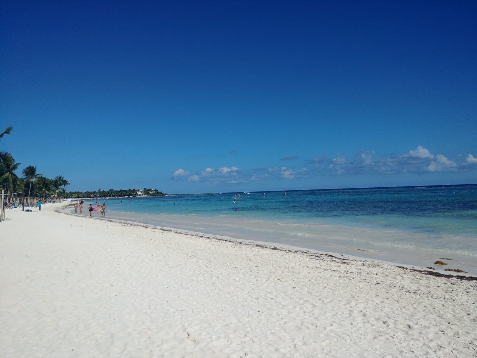 A beach with white sand, clear blue water, and palm trees.