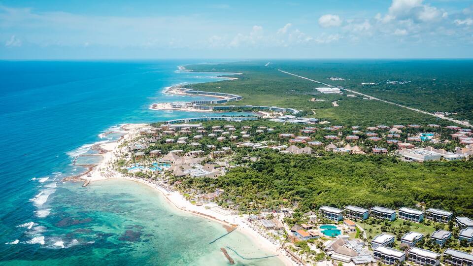 An aerial view of a coastal resort with a beach, clear blue waters, and lush greenery.