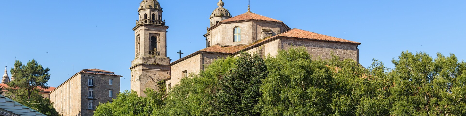 Una iglesia histórica con dos torres y un campanario, rodeada de árboles y un camino adoquinado.