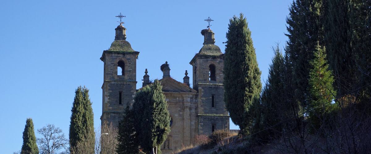 A historic church with two bell towers and a stone facade, surrounded by trees and a hillside.