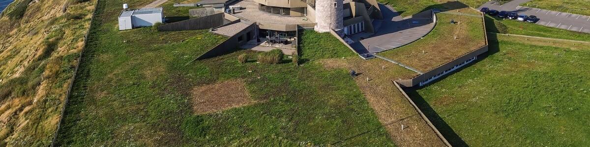 A lighthouse on a grassy hill with a clear view of the ocean.