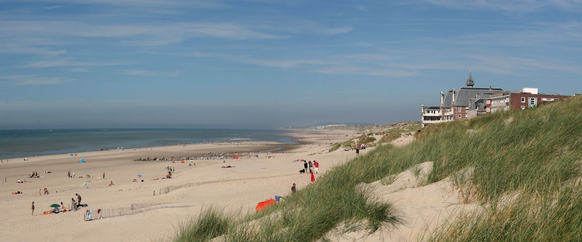 A sandy beach with people, tents, and a building with a spire.