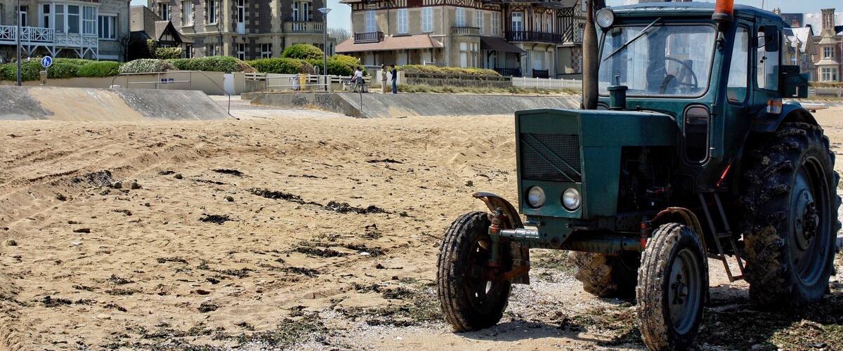 A green tractor on a sandy beach with historic buildings in the background.
