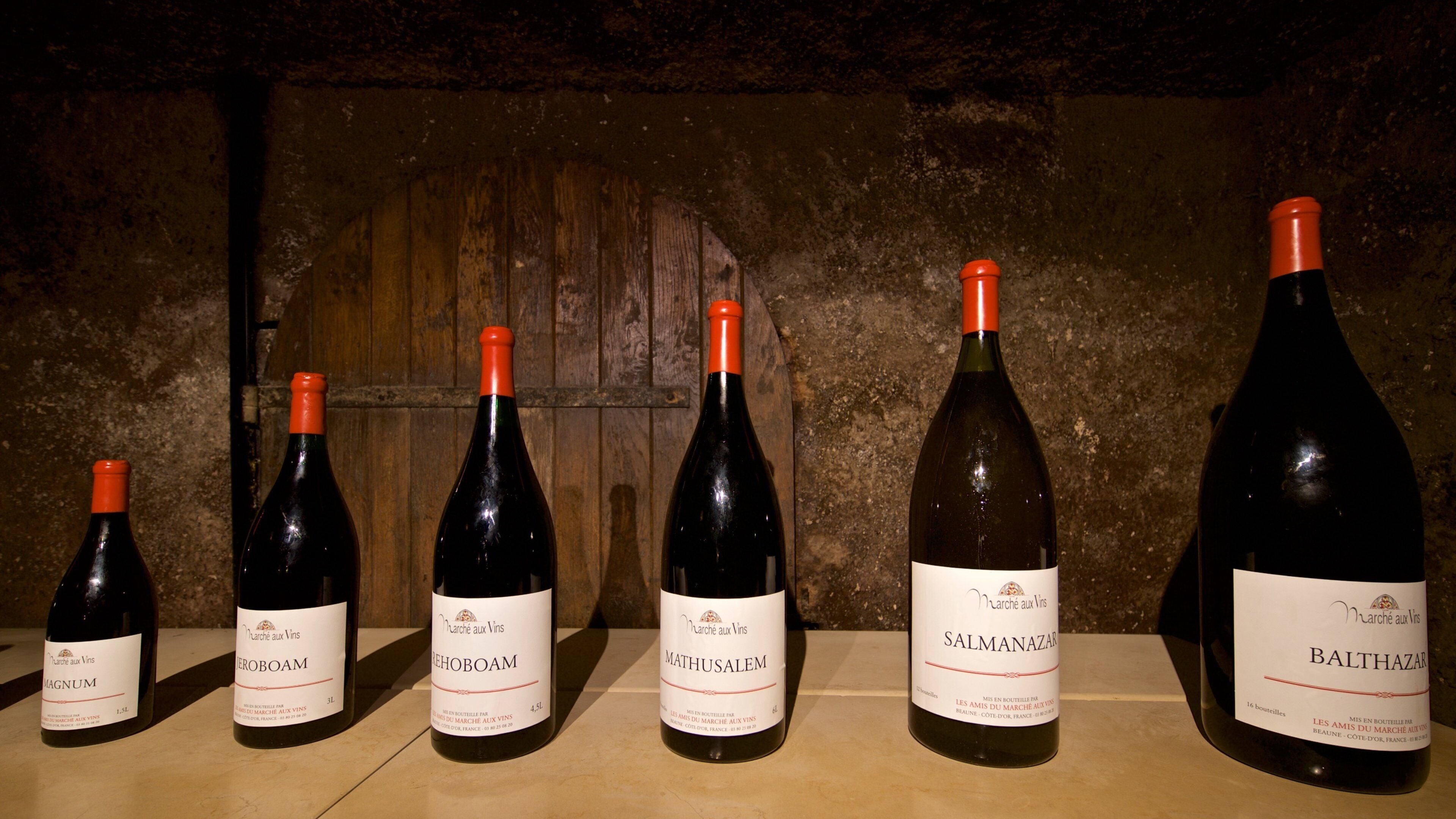 Cinco botellas de vino con etiquetas, sobre una superficie de madera frente a un fondo rústico.