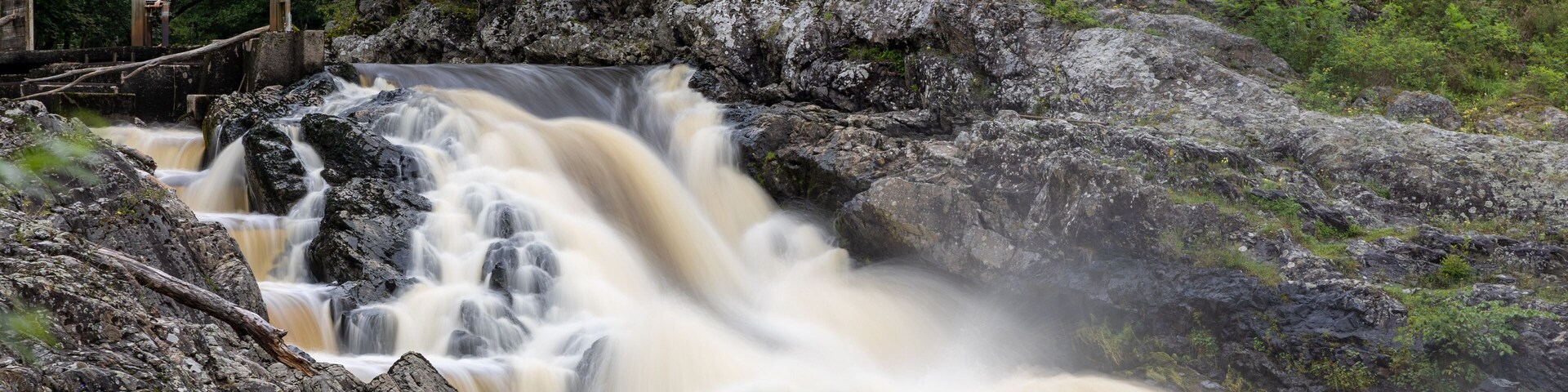 A waterfall cascading over rocks in a forested area with a bridge in the background.