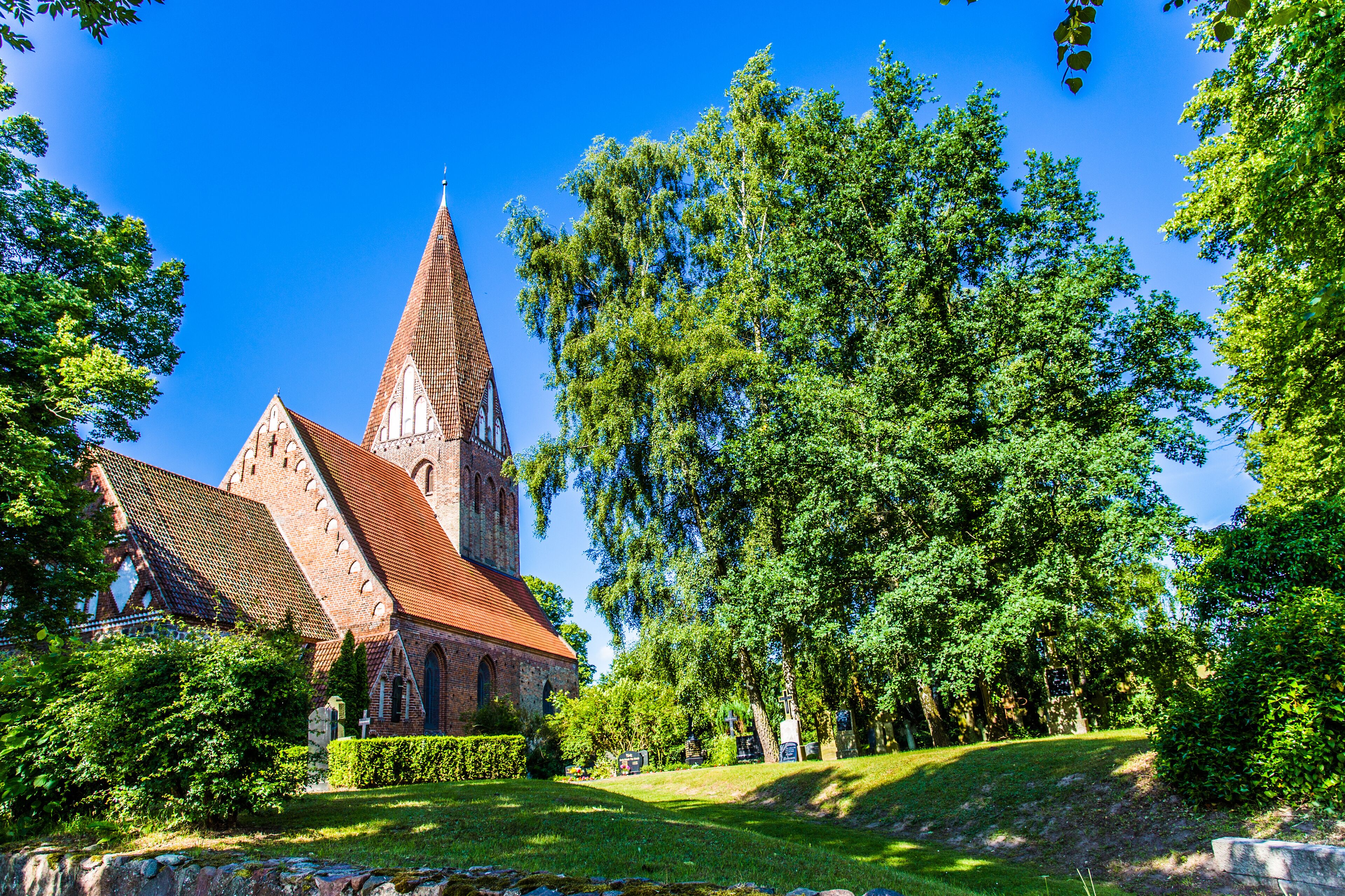 A church with a tall spire, surrounded by lush green trees and a well-maintained lawn.