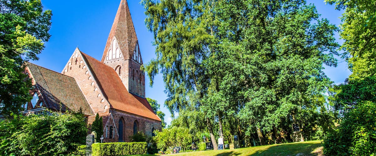 A church with a tall spire, surrounded by lush green trees and a well-maintained lawn.