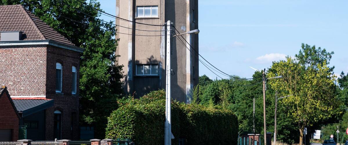 A tall water tower, a brick house, and a street with trees and a car.