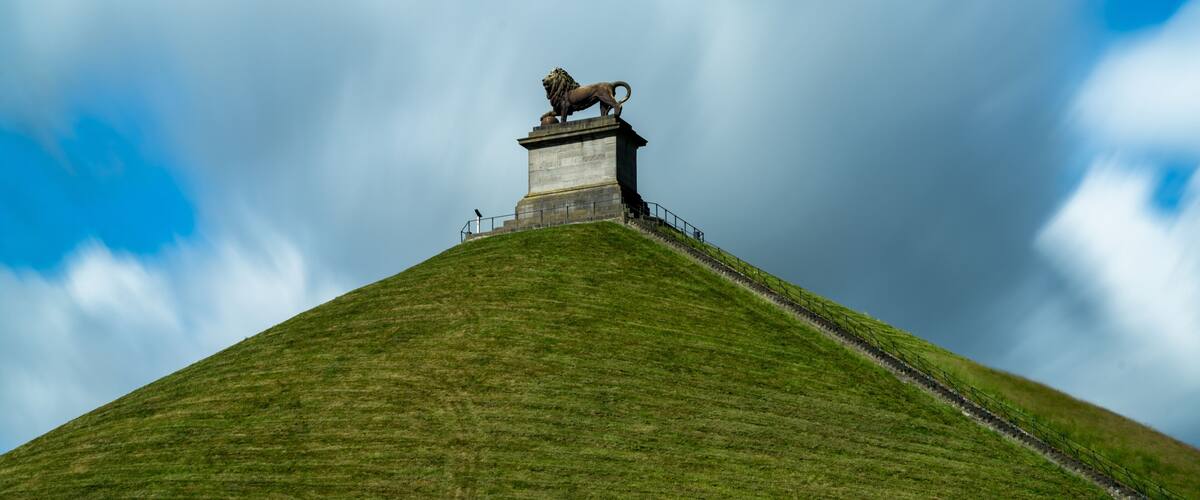 A grassy hill with a lion statue on top and a clear sky.