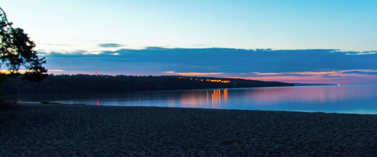 A beach with calm water reflecting lights from a distant shoreline.