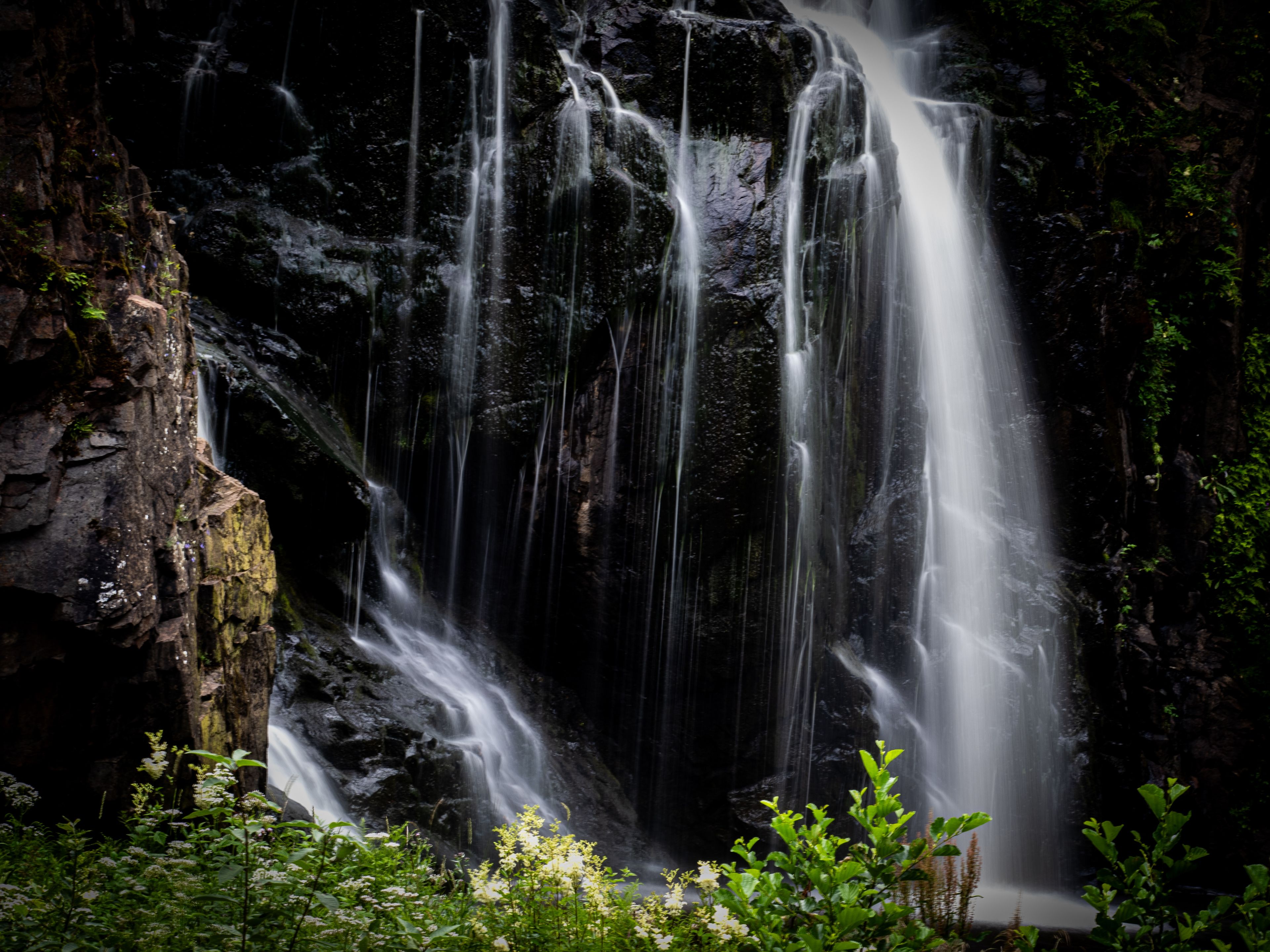 Uma cascata despencando por um penhasco rochoso, rodeada por vegetação exuberante.