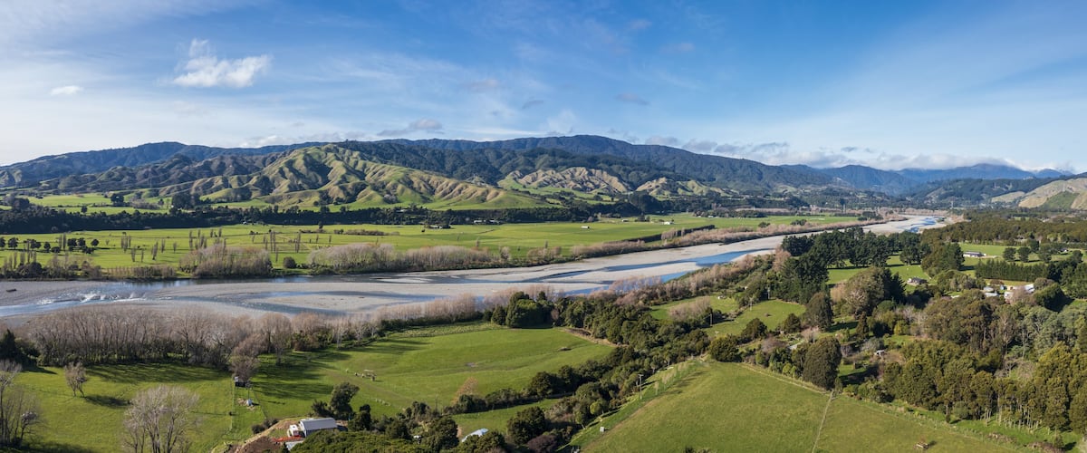A river winding through a valley with green fields and mountains in the background.
