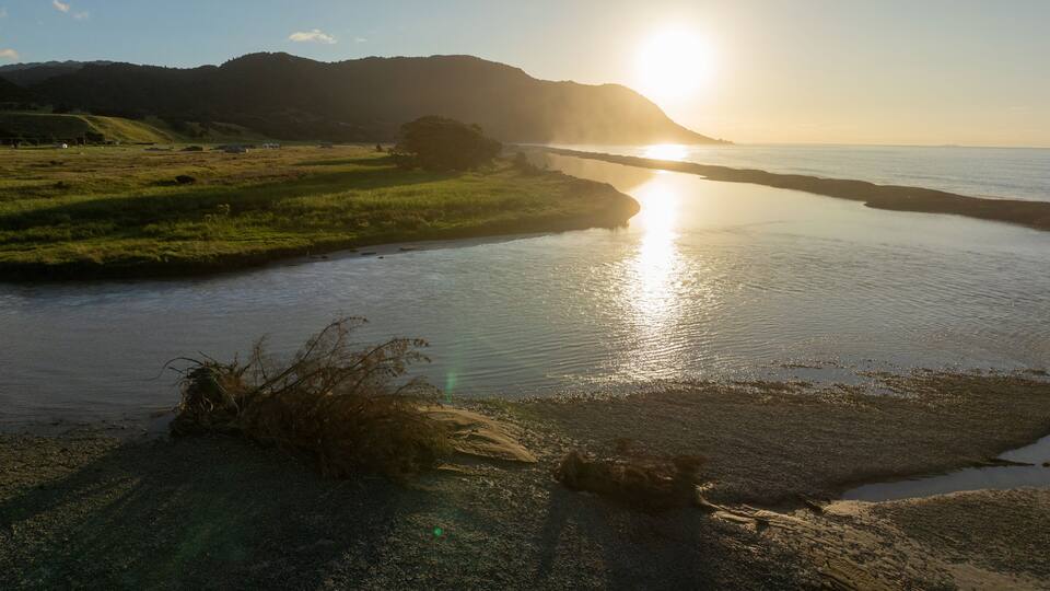 A river with a sunset, grassy banks, and distant hills.