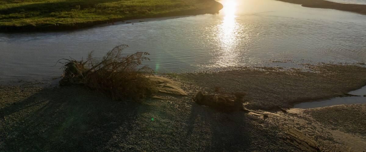 A river with a sunset, grassy banks, and distant hills.