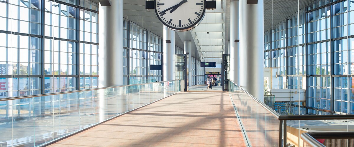 A spacious indoor area with large windows, a prominent clock, and a tiled floor.
