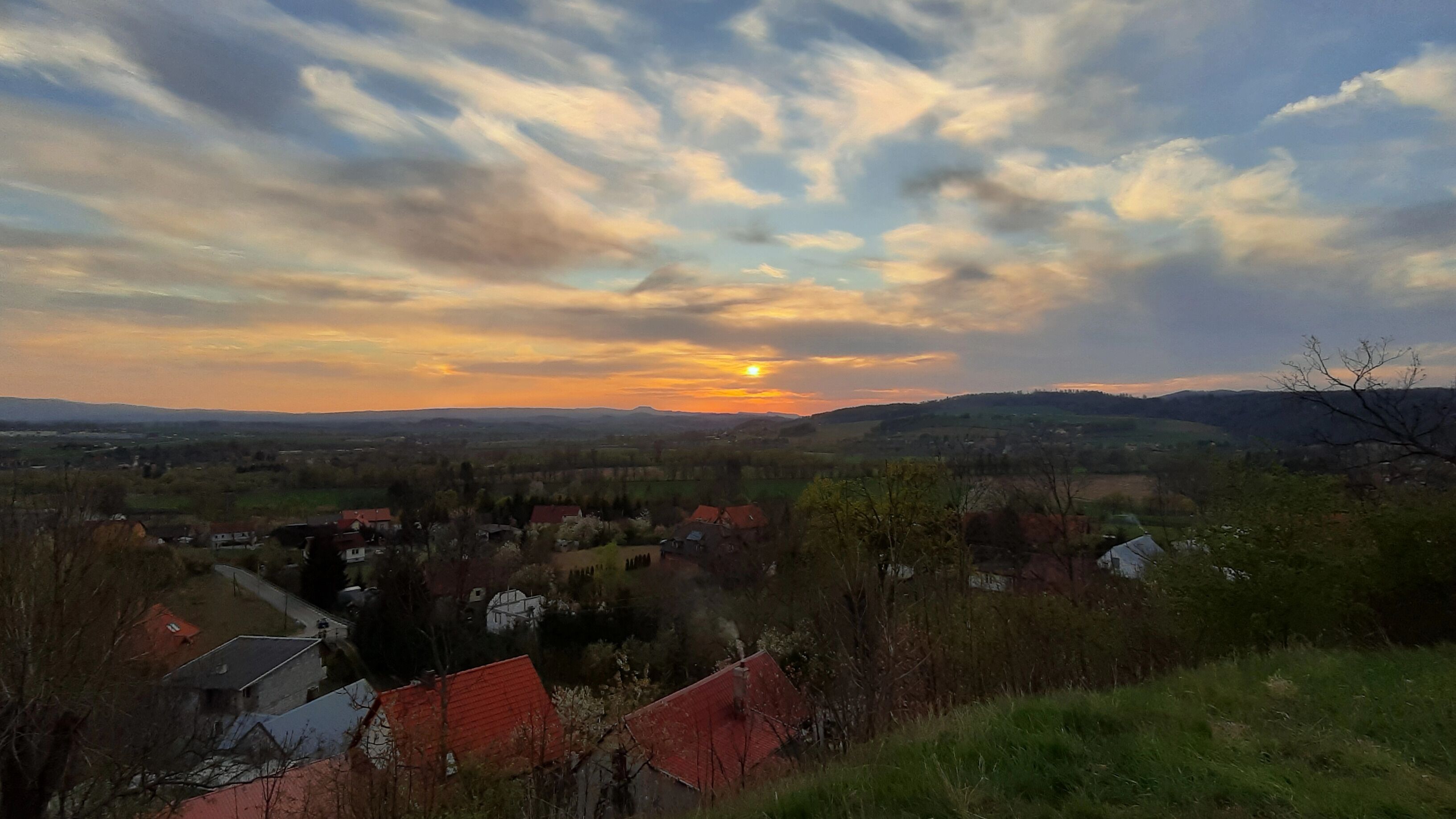 A sunset over a rural landscape with scattered houses and rolling hills.