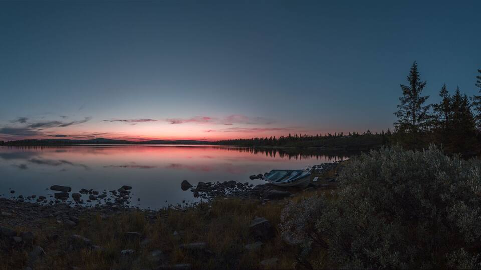 A calm lake at dusk with a sunset, surrounded by trees and a paddleboard.
