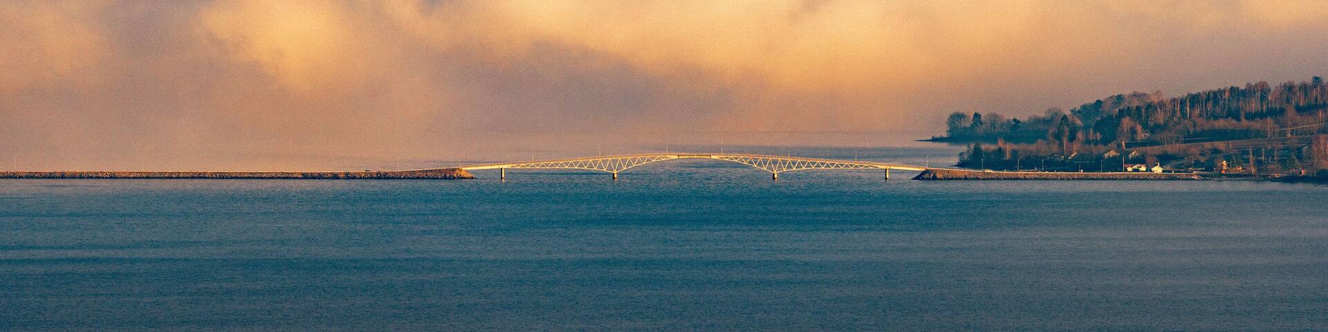 A bridge over a body of water with a forested hill in the background.