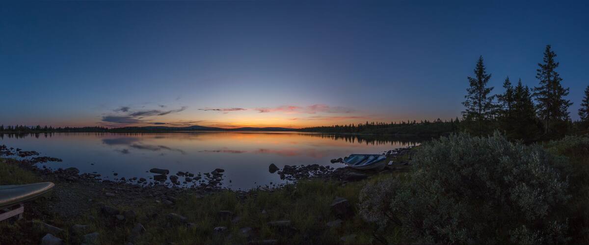 A calm lake at dusk with a sunset, surrounded by trees and a kayak on the shore.