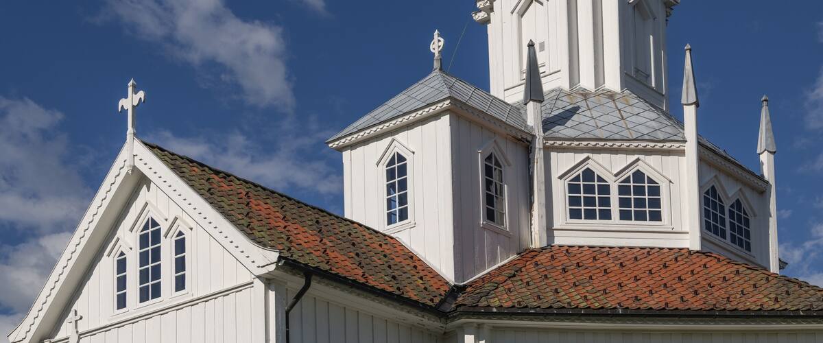 A white church with a red-tiled roof and a steeple against a blue sky.