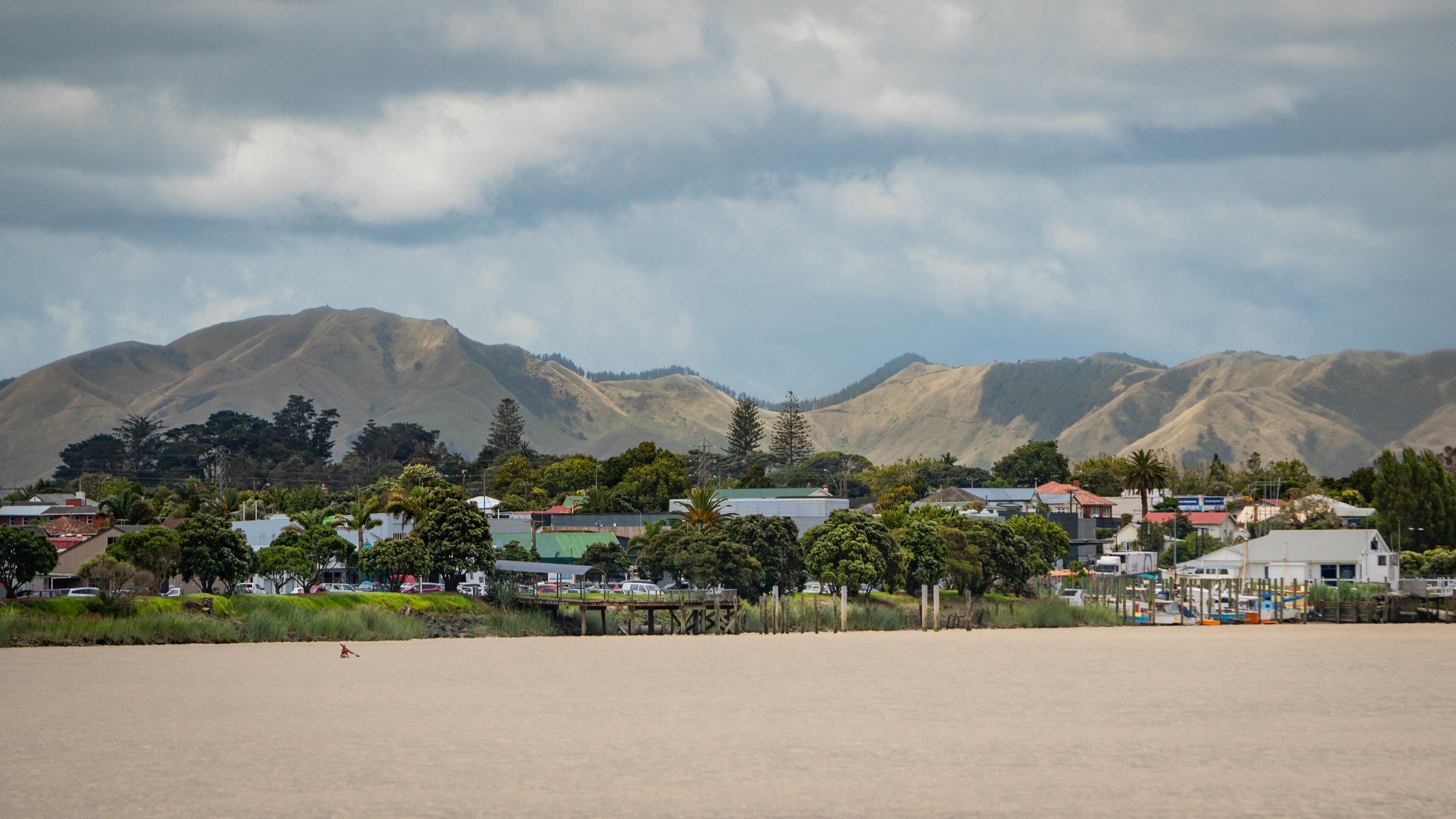 A coastal town with mountains in the background and a sandy beach in the foreground.