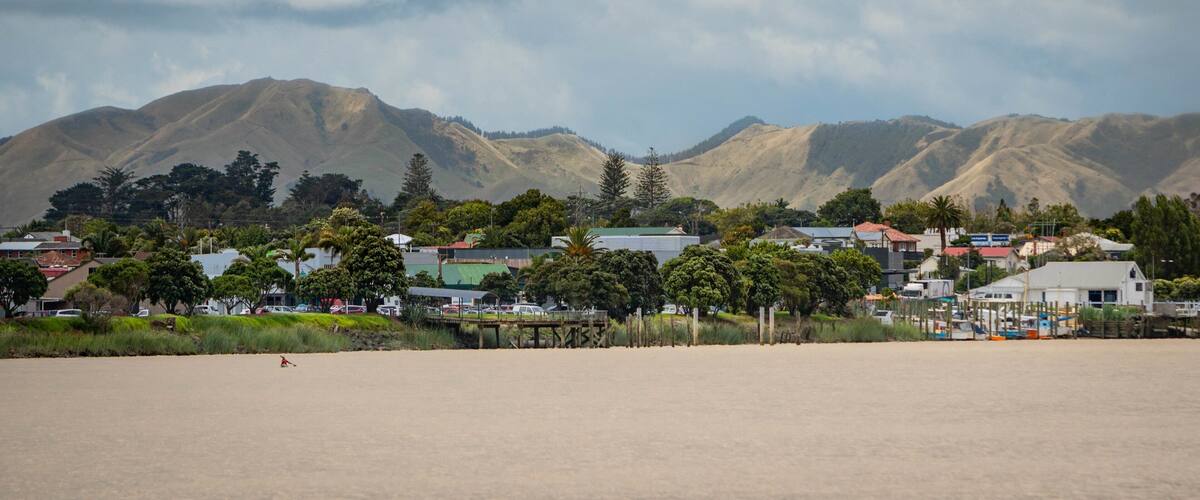 A coastal town with mountains in the background and a sandy beach in the foreground.