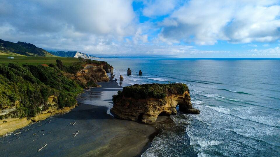 A coastal landscape with a prominent rock formation, a sandy beach, and a distant mountain range.