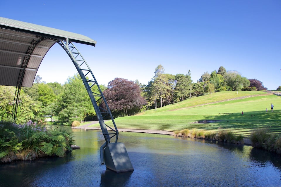 A bridge over a calm water body, surrounded by lush greenery and a well-maintained grassy area.