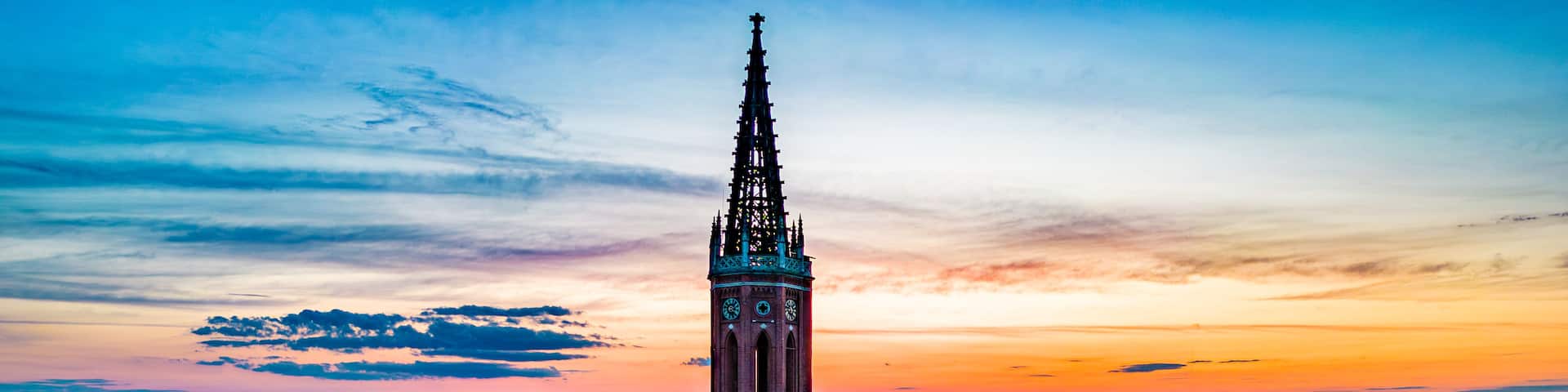 A church tower with a spire, surrounded by trees and buildings.