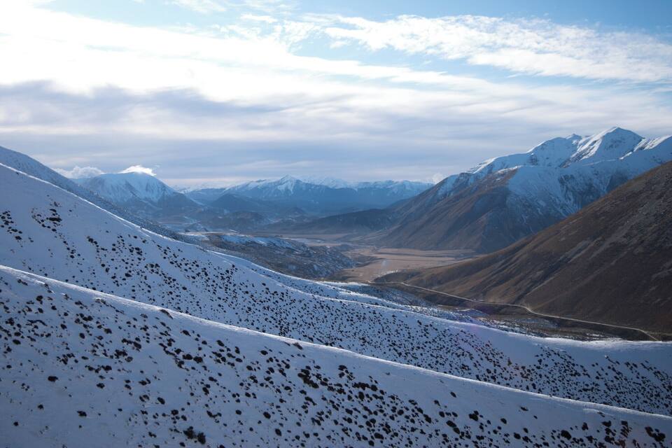 Cordillera nevada con un valle y una carretera.