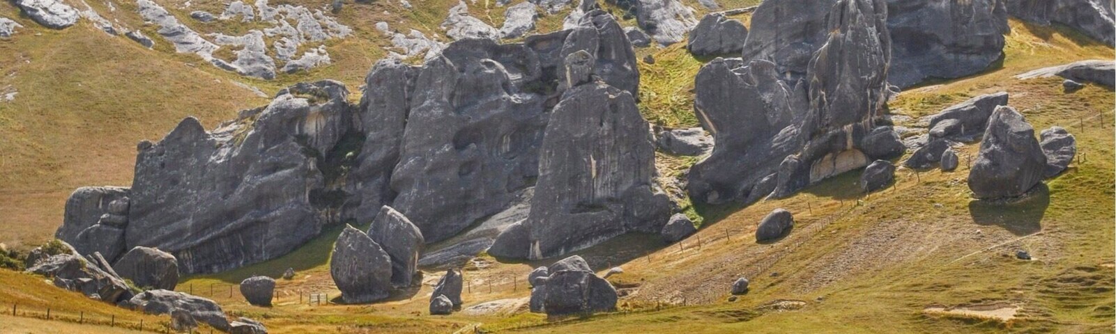 Un campo cubierto de pasto con vacas y grandes rocas sobre una colina.