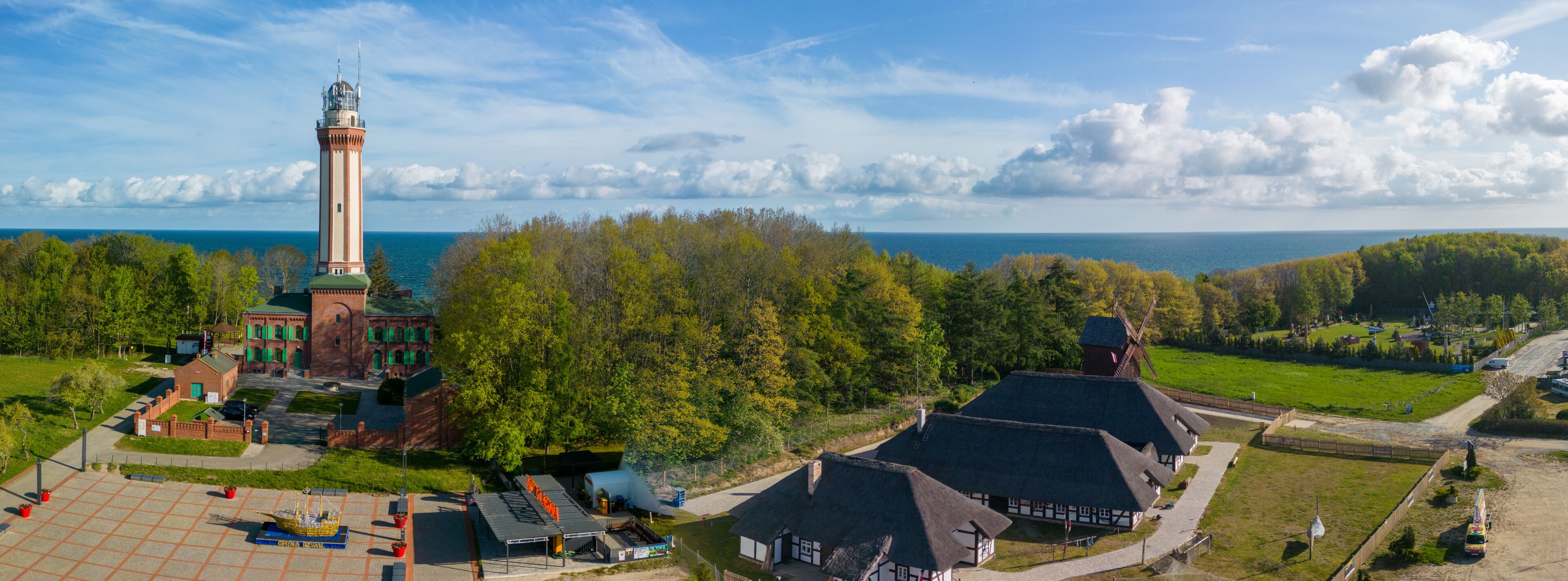 A lighthouse, traditional buildings, and a forested landscape with a view of the sea.