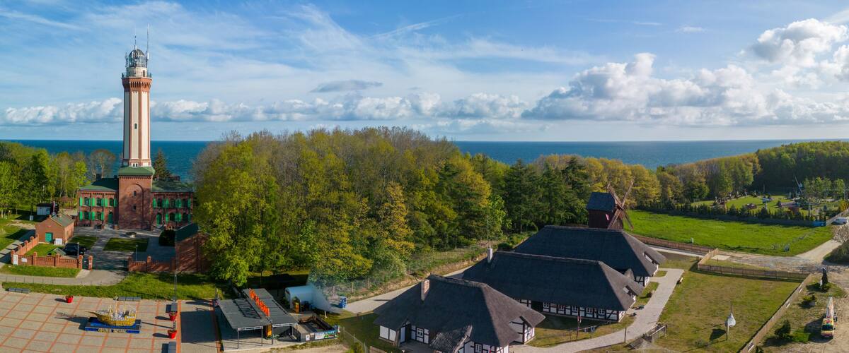 A lighthouse, traditional buildings, and a forested landscape with a view of the sea.