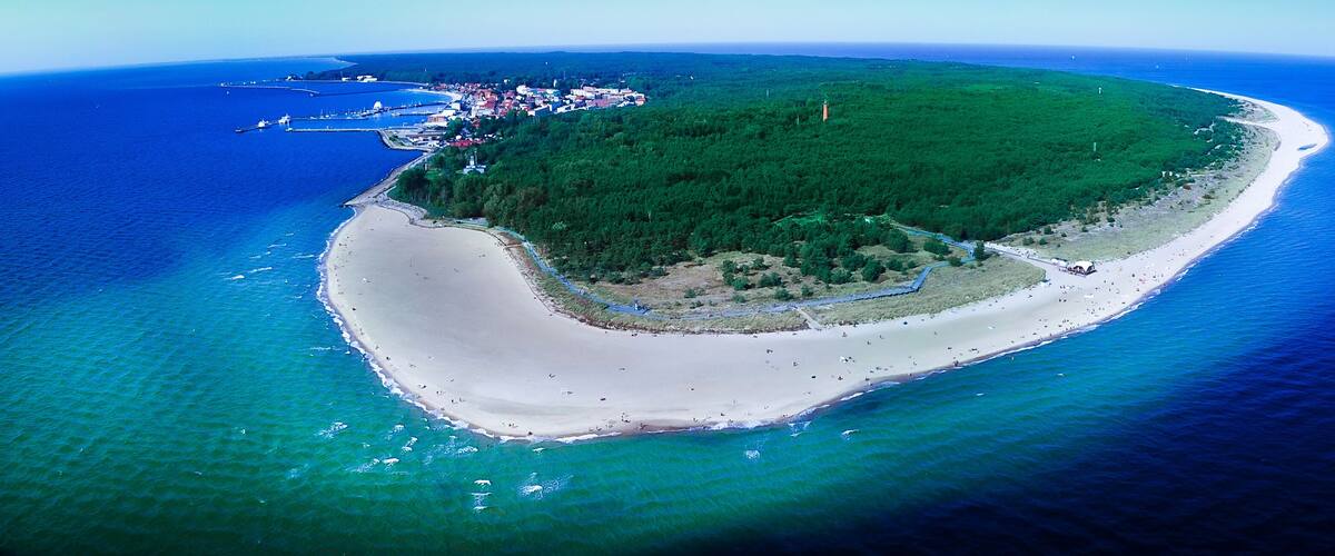 An aerial view of a tropical island with a white sandy beach, dense green forest, and a small town with buildings near the shore.