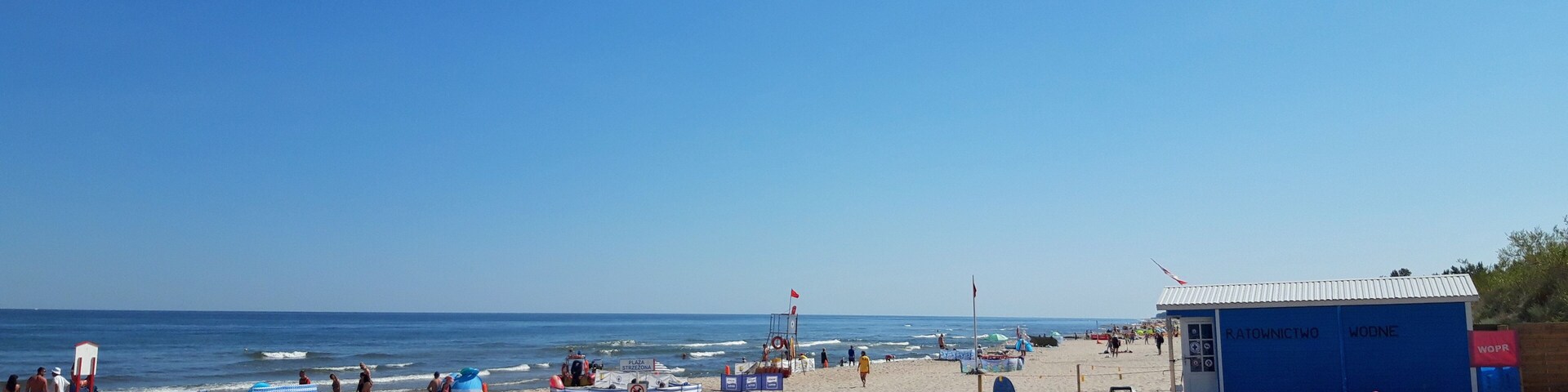 Una playa arenosa con albercas inflables, una torre de salvavidas y un cielo azul despejado.