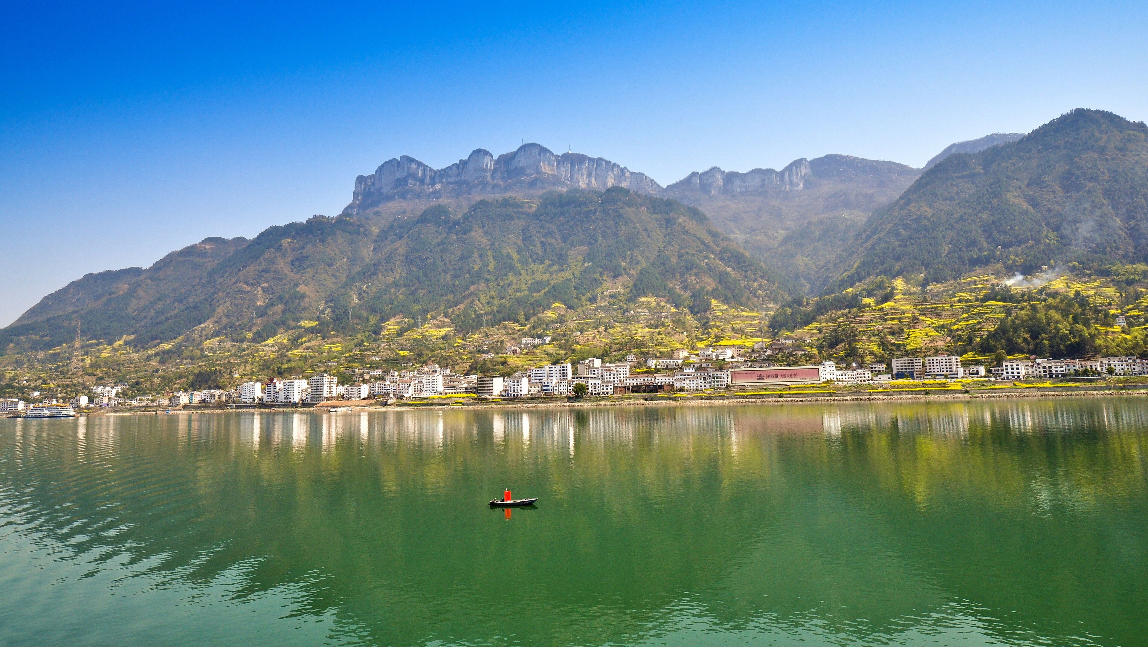 A calm lake with a boat, surrounded by mountains and a town with buildings.
