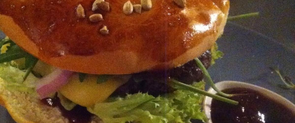 A burger with lettuce, tomato, and cheese, accompanied by tortilla chips and a small bowl of sauce.