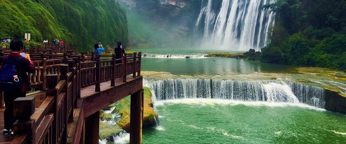 Un cascada que desemboiga sobre un penya-segat rocós a un riu, envoltada de vegetació exuberant.